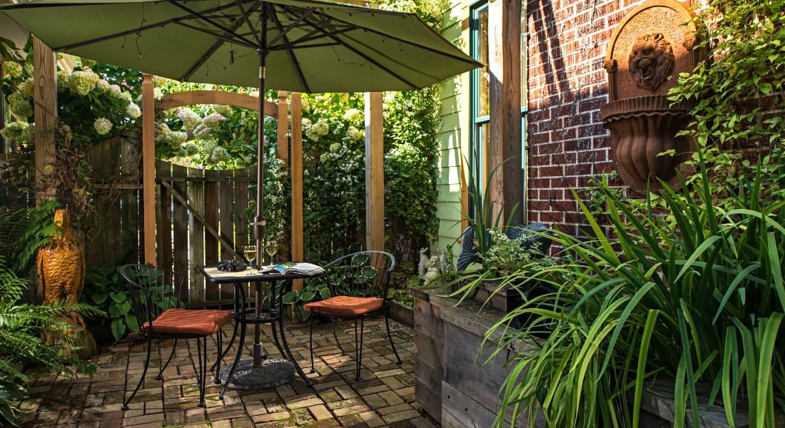 Outdoor area with brick pavement, a sitting table with an umbrella and two glasses of white wine