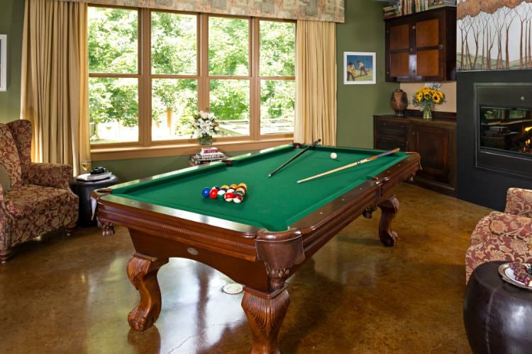 Interior room with a wooden pool table with green felt covering, two red floral chairs and a fireplace.