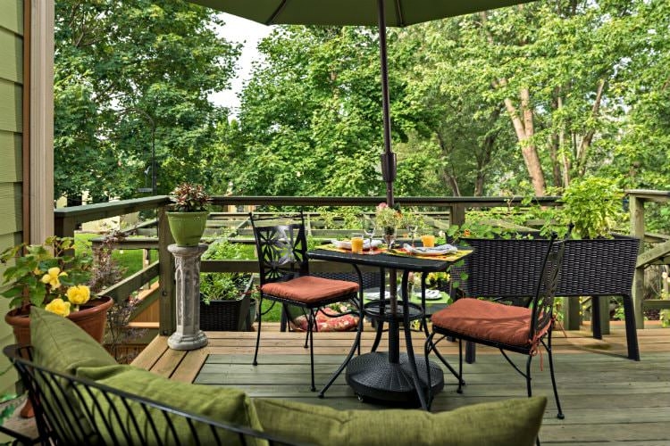 Outdoor wooden porch with a black table covered by a large green umbrella displaying a breakfast spread