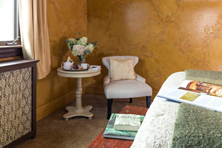 Guest room with a curtain covered window, a cream wooden table and small leather reading chair.