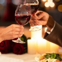 A couple clinking wine glasses while having dinner at a restaurant