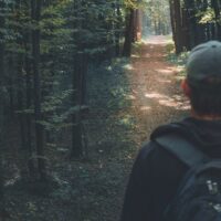A man stands before a path in the woods on a hike