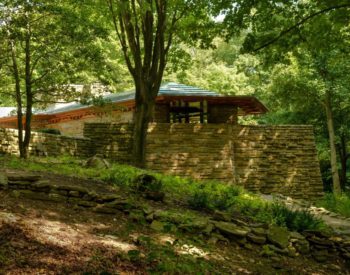 Usonian stone house in a woodland setting with trees and grasses.