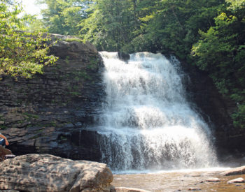 Large, three tiered waterfall, cascading down granite ledges next to rhododendron bushes