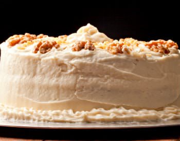 A round two-layered cake with a thick white icing and sprinkled on top with nuts.