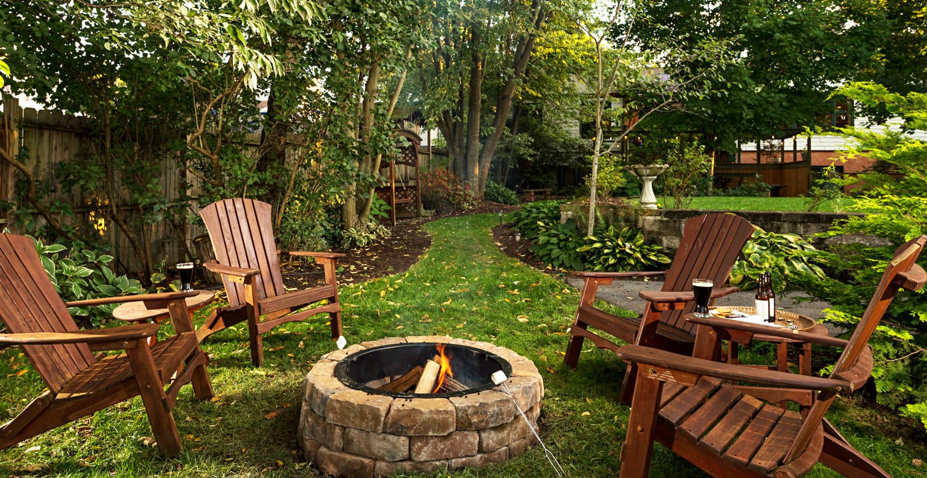 Outside view of a grassy backyard, several lawn chairs around a stone fireplace, a green path leading away from scene