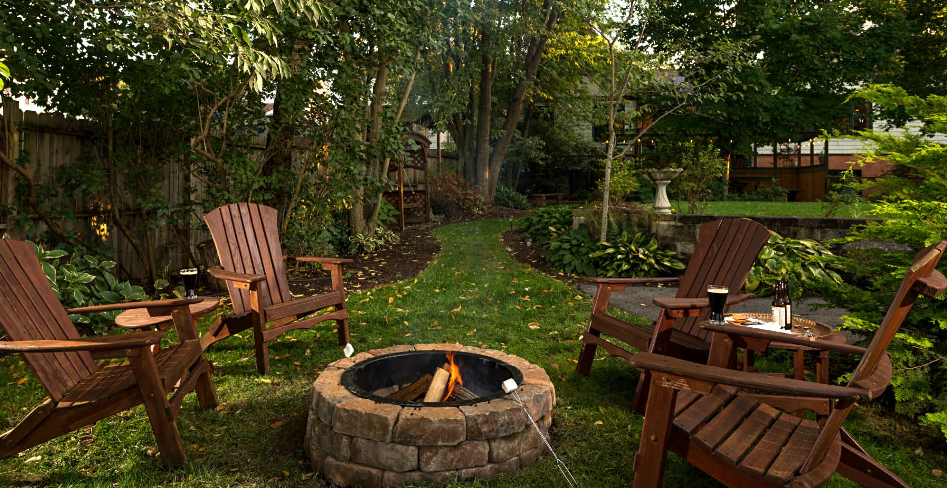 Outside view of a grassy backyard, several lawn chairs around a stone fireplace, a green path leading away from scene