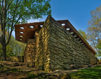 Exterior view of a tall, angular stone building amongst trees and surrounded by patchy green grass