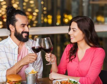man and woman smiling at each other clinking wine glasses while dining out