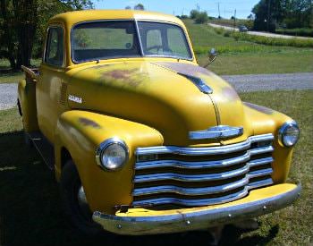 Old time car painted yellow with some brown rust spots in the paint parked on green grass