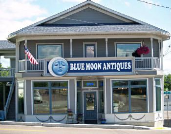 exterior view of Blue Moon Antiques, a grey two story building with white detailing on a street with an incline