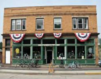 An exterior view of a vintage brick building with a green storefront on display, bikes parked in racks out front.