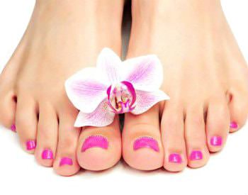 A pair of freshly manicured feet with bright pink toenail polish and a flower on top of the feet.