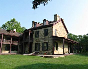 Outdoor view of an old cottage styled building, stone foundations with wooden porches and roofing.