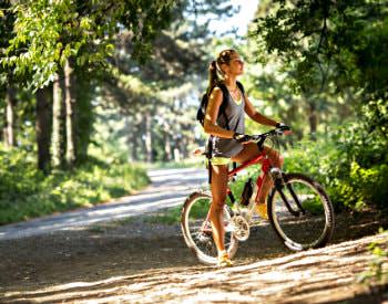 An outdoor trail winding through the thick green woods, a woman on a bike pulled off to the side.