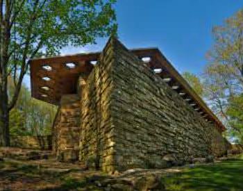 Exterior view of a tall, angular stone building amongst trees and surrounded by patchy green grass