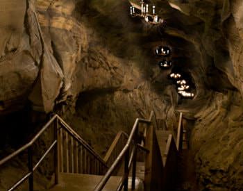 Deep tunnel through a grey, dimly lit cave and a staircase running along the bottom