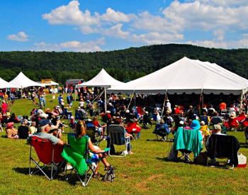 Exterior view of the Laurel Hill Bluegrass festival people sitting in lawn chairs and under several white tents.