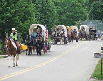 Street view of the National Road Festival, a line of covered wagons filled with people in old western outfits.