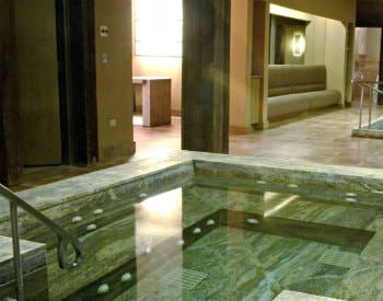 Indoor view of the Nemacolin Spa, a crystal clear spa bath with grey walls and lined in white water jets.