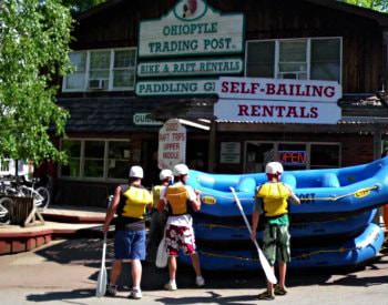 Exterior view of Ohiopyle Trading Post, a wooden building with a stack of blue river rafts out front.
