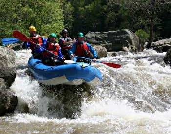 A blue river raft full of people going over a slight drop in a fast moving river