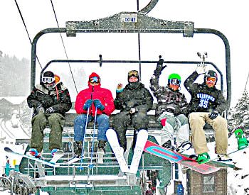 Five people sitting on a ski lift waving, surrounding by thick white snow fall.