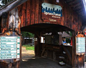 Exterior view of a brown bridge covering with a blue sign that reads “Spruce forest artisan village”