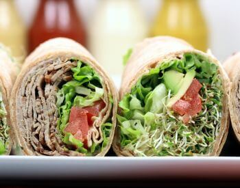 wraps with meat, lettuce and tomato on whit plate with blurred condiments bottles in background
